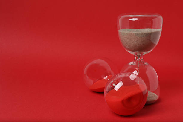 Hourglass with flowing sand against red background. Space for text