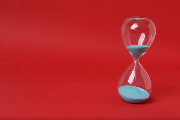Hourglass with flowing sand against red background. Space for text