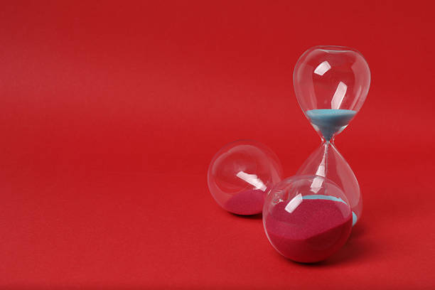 Hourglass with flowing sand against red background. Space for text