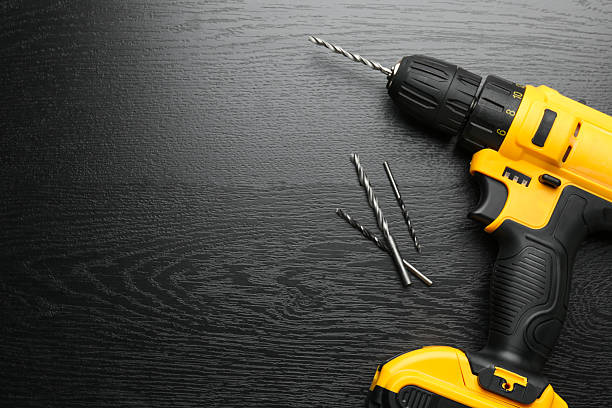 Cordless electric drill and bits on black wooden table, flat lay. Space for text