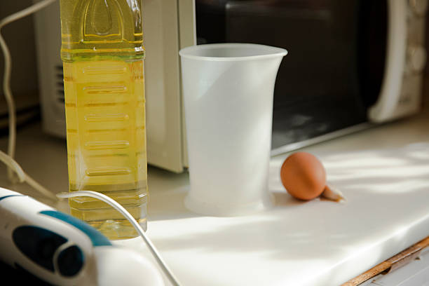 Plastic measuring container placed on a kitchen counter during the preparation of homemade mayonnaise. Simple tools and natural ingredients used in traditional home cooking.