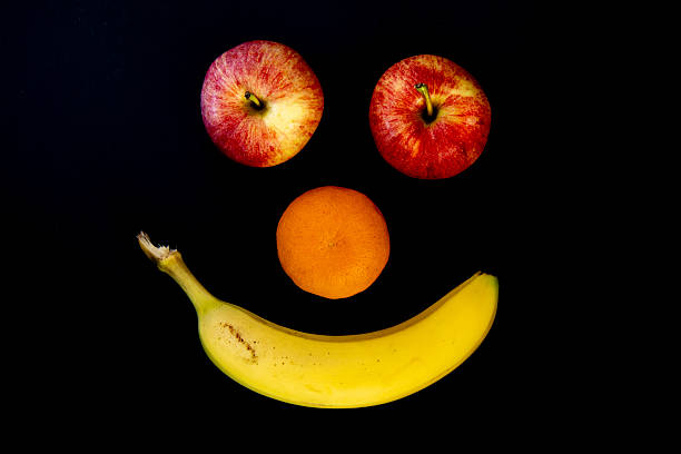 Two red apples for eyes, one orange for the nose, and one yellow banana for the mouth to create a smile using fruit