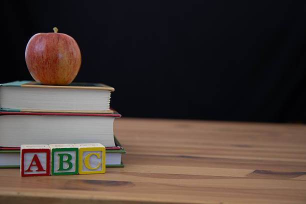 Desk with three books stacked on the left side with a red apple on top and wooden ABC blocks in front