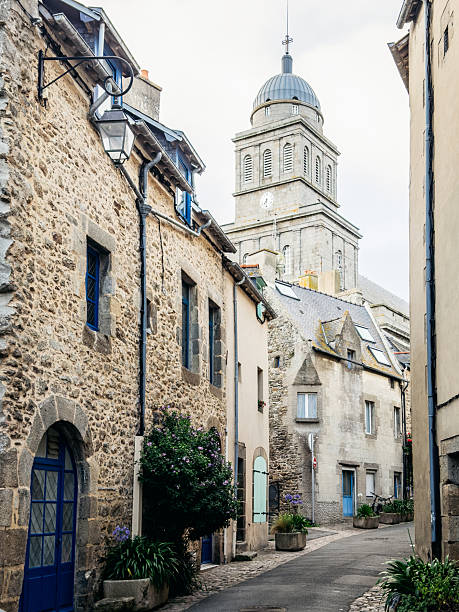 A narrow cobblestone street lined with historic stone houses leads toward a church tower in Saint-Malo, Brittany, illustrating everyday life in a preserved French coastal town.