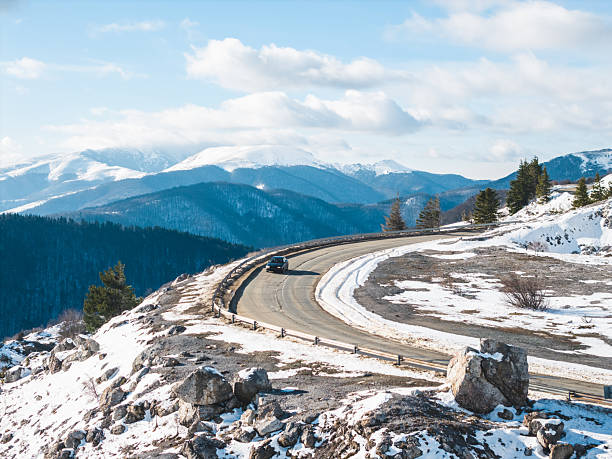Car driving along a snowy road toward a mountain pass during winter. Scenic travel and journey concept symbolizing adventure, freedom, and seasonal exploration.