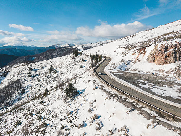 Scenic winter drive showing a car moving toward a mountain pass surrounded by snow-covered landscape. Travel and adventure concept with cold seasonal atmosphere.