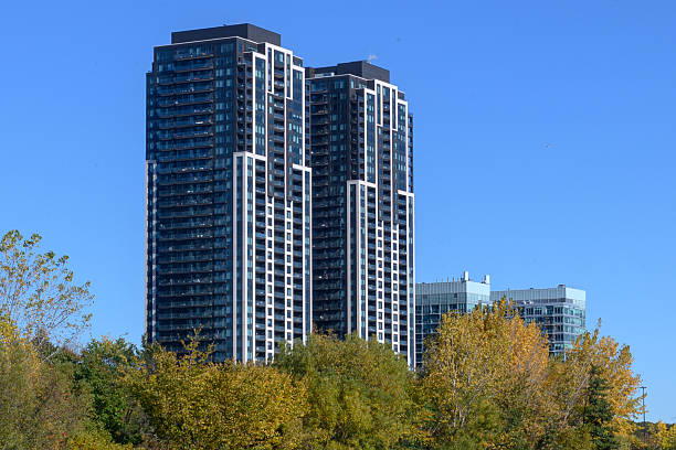 Contemporary high-rise residential buildings rising above vibrant autumn trees under a clear blue sky, illustrating urban development and nature within the cityscape of Etobicoke, Canada