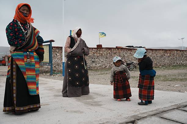 Two Tibetan children and their parents standing on a village road in western Tibet, wearing traditional clothing and hats.