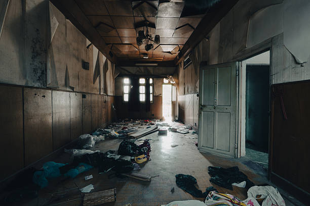 Immersive photograph of a dimly lit, long abandoned corridor featuring damaged ceilings with hanging fixtures, scattered clothing, bags, papers, and debris across the floor, multiple open doorways revealing further ruin, and soft light spilling from windows and rooms. This immersive image powerfully conveys desolation, mystery, and the eerie stillness of a once-occupied space, perfect for horror, thriller visuals, documentary series, psychological themes, or atmospheric stock use. High-resolution capture with rich tonal depth, intricate details of decay, and leading lines that draw the viewer deeper into the scene. Keywords: abandoned corridor hallway, derelict building interior, scattered belongings ruin, damaged ceiling decay, eerie long passage, urban exploration hallway, post-apocalyptic corridor, haunting abandoned space, light through doors photo, atmospheric ruin exploration.
