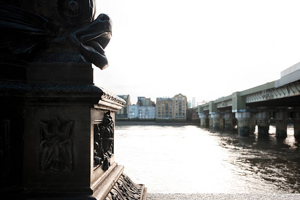 Sturgeon fish sculpture on an old street lamp overlooking the river thames and southwark bridge, weathered metal detail in a london cityscape, sunny day, foreground focus