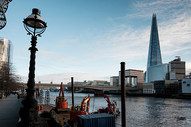 Iconic modern skyscraper the shard towering over london's urban landscape, with the river thames flowing below, showing construction activity and a vintage street lamp in the foreground