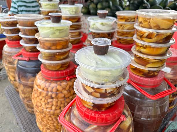 Assorted pickled fruits and vegetables inartem  displayed in clear containers at a vibrant street food stall.
