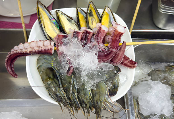 A white plate filled with a variety of seafood, including shrimp, squid, and octopus. The shrimp are in the center of the plate, while the squid and octopus are placed on the sides