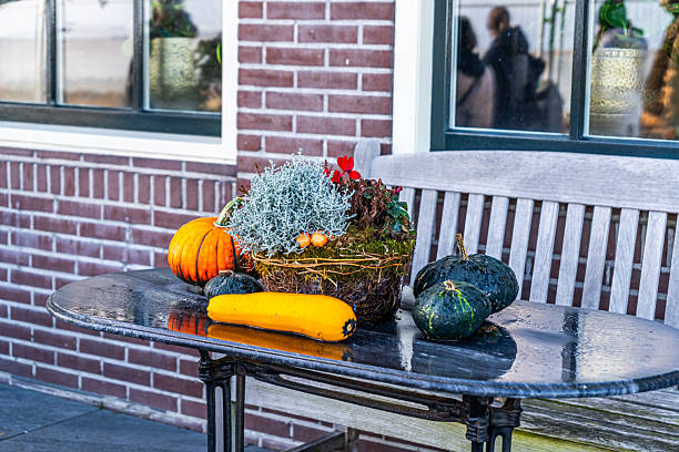 Pumpkins on table with flowers plant. Halloween and Thanksgiving decorations. Fall decor at home garden. Autumn harvest