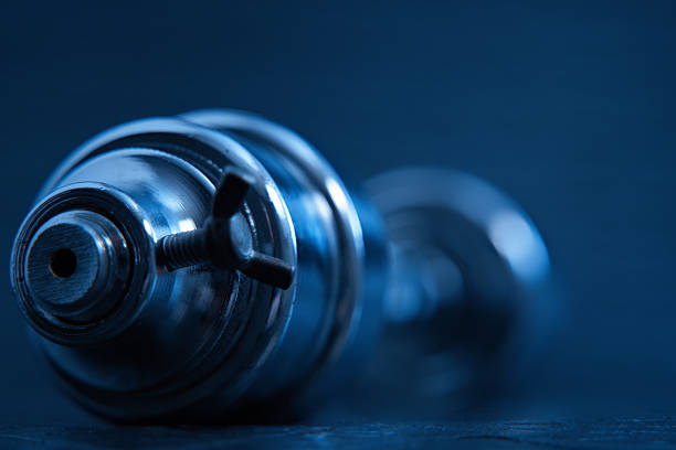 Chrome dumbbell showing adjustable weight plates in blue light on a dark surface