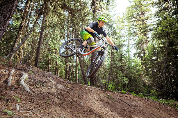 Energetic cyclist performing a jump on a mountain bike in a lush green forest. Highlighting the joy of outdoor adventures, biking challenges, and exploring nature on two wheels.
