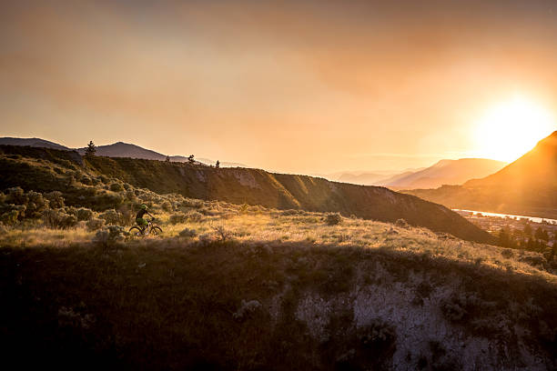 Distant view of mountain biker riding grassy hills at sunset, Kamloops, British Columbia