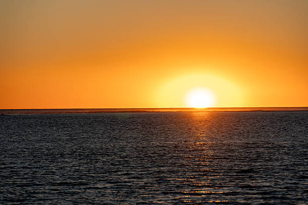 Stunning orange sunset glowing above endless ocean horizon casting warm light across water surface creating peaceful marine atmosphere.