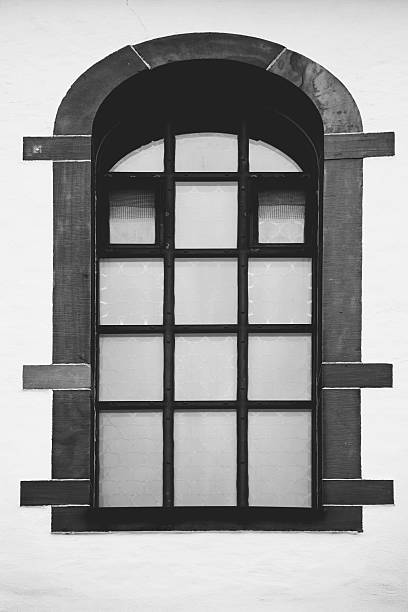 Historic arched window with metal bars and stone frame on a white wall, creating a minimalist architectural composition with strong symmetry and contrast.