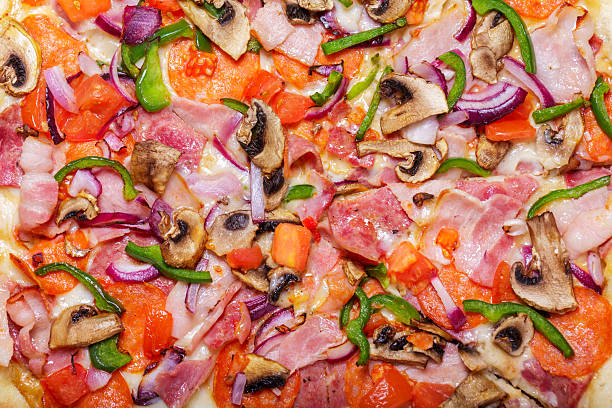 close up of pizza with ham, pepperoni and vegetables as background, top view
