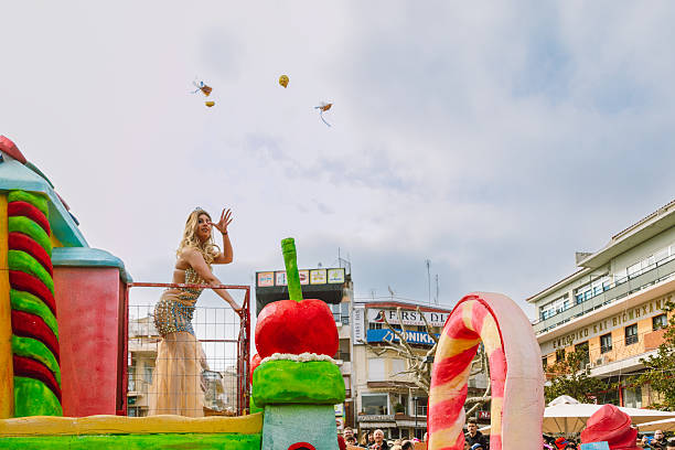 Xanthi, Greece - February 18, 2018: A colorful carnival float moves through the city center of Xanthi during the annual Apokries carnival celebrations as a female performer in an ornate costume stands on the float and throws small gifts to the crowd while thousands of spectators gather along the streets near the iconic clock tower to watch the festive parade featuring music costumes and themed floats
