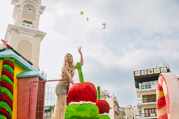 Xanthi, Greece - February 18, 2018: A colorful carnival float moves through the city center of Xanthi during the annual Apokries carnival celebrations as a female performer in an ornate costume stands on the float and throws small gifts to the crowd while thousands of spectators gather along the streets near the iconic clock tower to watch the festive parade featuring music costumes and themed floats