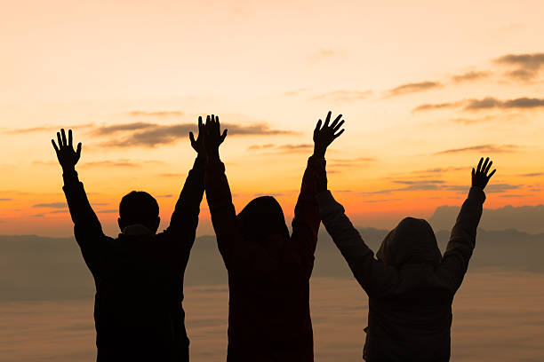 istock Silhouetted friends raise hands in celebration at sunrise on a mountain peak, overlooking a sea of fog. A conceptual image of teamwork, success, freedom and friendship in nature's beauty. 2256864107