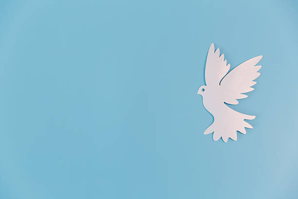 White paper cut dove on a blue background. This minimalist flat lay represents peace, hope and faith, featuring wide copy space for international peace day or humanitarian concepts.