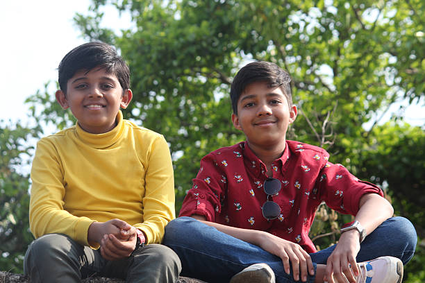 Two dark-haired Latino male children sitting on the ground in a park living in poverty without toys, dream, play, imagine a happy childhood