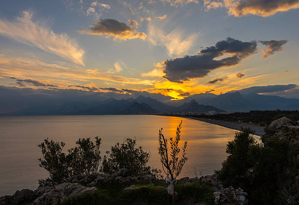 Golden sunset reflecting on calm sea along a curved coastline with mountains in the background