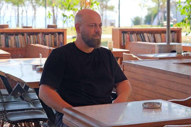 Man Waiting to Order at a Bar Table During Daytime. Daytime Bar Scene with Man Waiting for Service. Customer Sitting at Bar Table Waiting to Order.
