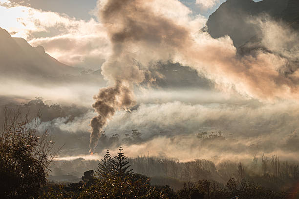 Smoke and haze fill a mountain valley as fires burn during a riot. The early morning light reveals layers of mist and drifting smoke against rugged mountain terrain, documenting the environmental impact of civil unrest