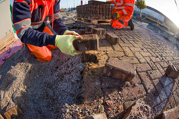 Two workers are on a construction site laying bricks on a path. They are focused on their task, with tools and materials nearby as they work under the sun.