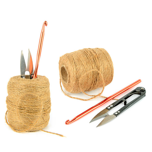Spools of natural jute twine are paired with a bright orange crochet hook and metal snip scissors. This clean studio shot on a white background offers copy space for hobby and craft designs.