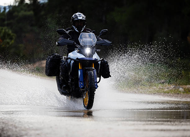 Motorcyclist splashing through a large water puddle on a wet road