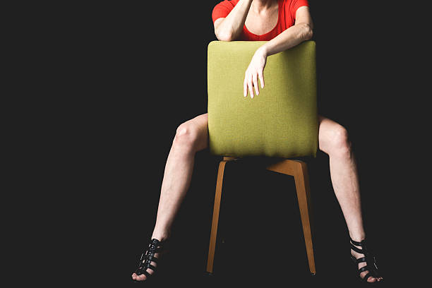 A woman in a red shirt adopts a bold seated posture on a green chair in a dark studio setting, emphasising strength and presence.