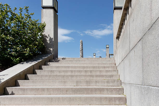 Oslo, Norway - May 18, 2025: Steps ascend towards Vigeland Park, featuring a stone monolith and lush greenery under a clear blue sky