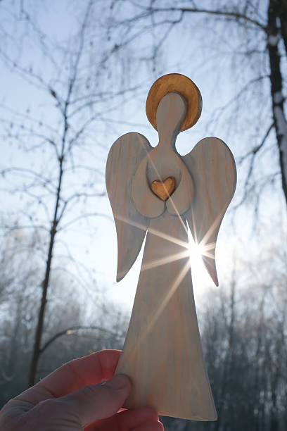 Angel wooden figurine through which a sun ray passes. Guardian angel in a woman's hand. Hope, faith, and love concept.