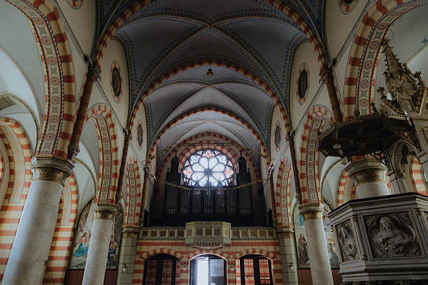 Intricate church interior showcasing gothic architecture with high arched ceilings, ornate pillars, a stunning rose window, and a pipe organ
