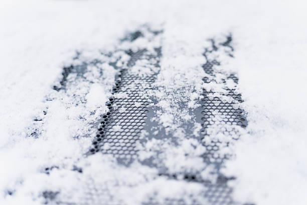 Snow covered perforated metal grid in macro view, soft focus winter texture with scattered ice crystals forming abstract pattern on dark surface