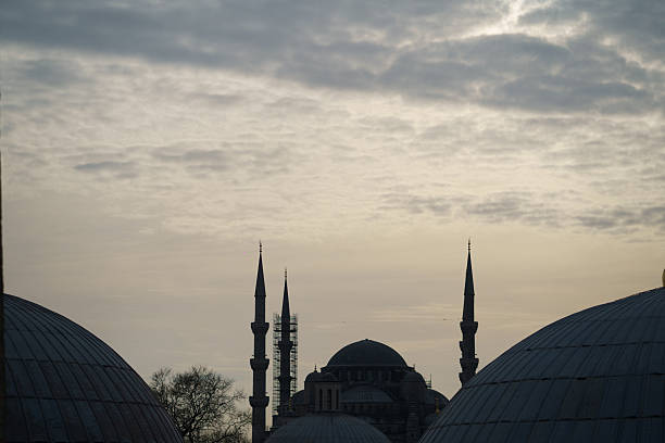 Sultan Ahmed Mosque in Istanbul, Turkey, with minarets and domes silhouetted against a dramatic cloudy sky at sunrise