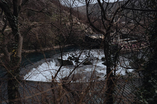 Buna River waterfall cascade flowing downstream, surrounded by bare winter trees and rocky mountains in Blagaj, Bosnia and Herzegovina