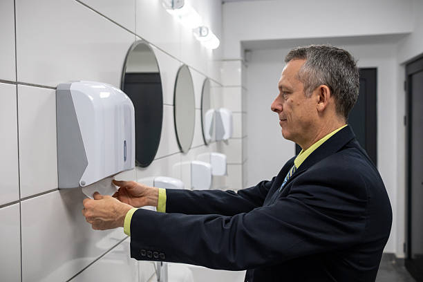 A businessman in a suit stands at a hand dryer in a sleek, modern bathroom, highlighting hygiene practices in professional environments and promoting cleanliness in public restrooms.