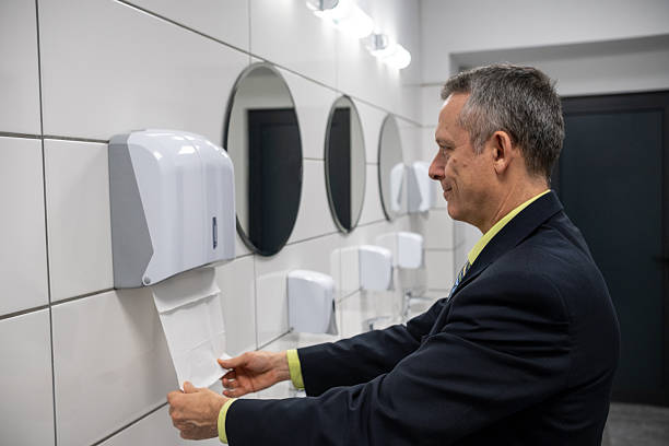 A businessman in a suit stands at a hand dryer in a sleek, modern bathroom, highlighting hygiene practices in professional environments and promoting cleanliness in public restrooms.