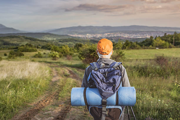Senior birdwatcher wearing backpack is enjoying his retirement by hiking through nature, using trekking poles and binoculars looking for rare birds.