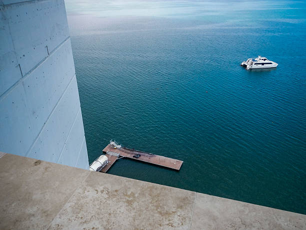 High-angle view from a modern waterfront building in Panama City overlooking calm coastal waters. A small private dock and a motor yacht are visible below, illustrating urban waterfront living, marina infrastructure, and contemporary coastal real estate in daylight.