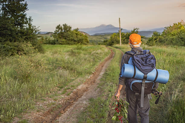 Senior birdwatcher wearing backpack is enjoying his retirement by hiking through nature, using trekking poles and binoculars looking for rare birds.