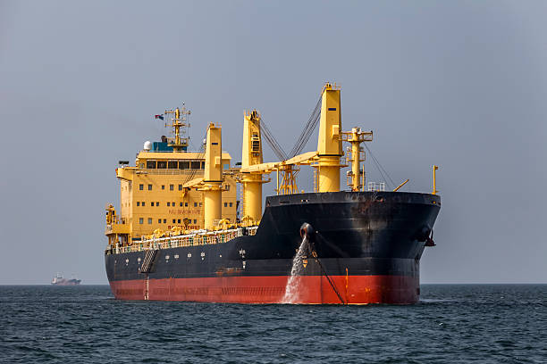 Large cargo ship anchored at sea while waiting to enter the Panama Canal. The vessel is seen from the front with visible ballast water discharge, illustrating global shipping, maritime logistics, and international trade in daylight conditions.