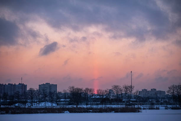 sunset over a winter city with clouds in the sky and a sun pillar extending into the sky