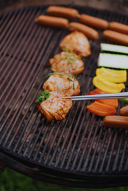 Grilling chicken thighs with vegetables and sausages on barbecue